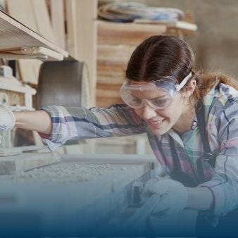 Eine junge Frau mit Schutzbrille arbeitet an einer Werkbank.